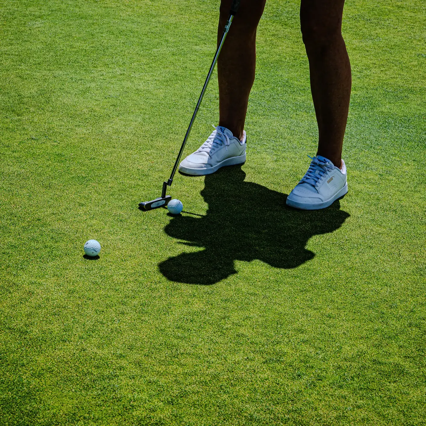 A golfer lining up a putt beside two golf balls on a vivid green